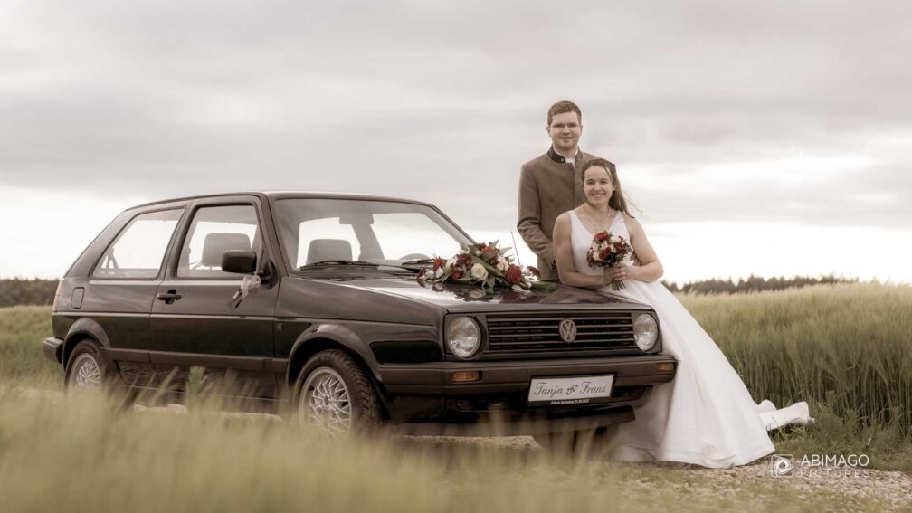 Lächelndes Brautpaar lehnt sich am Hochzeitsauto an, Alt-Filter, Braupaar, Hochzeit, Getreidefeld
